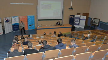 Osoba przemawiająca podczas konferencji EKO JURA. Widok na salę i osoby uczestniczące w konferencji z dalszych rzędów. 